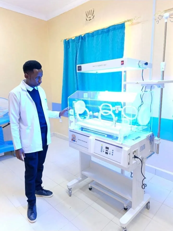 A healthcare professional beside an infant incubator and phototherapy equipment.